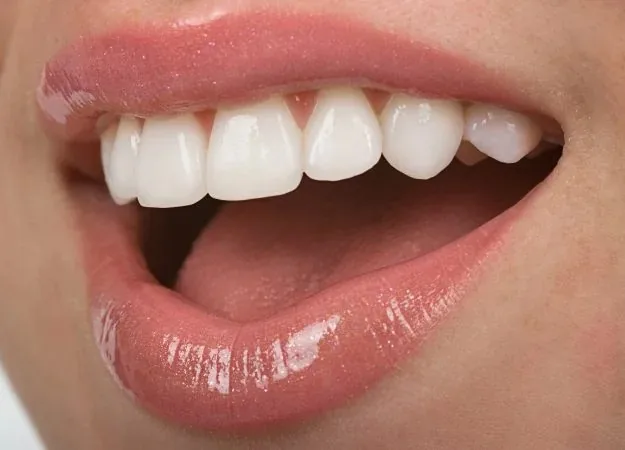 Close-up of a person's smiling mouth showing upper teeth with glossy pink lips.